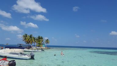 Boat on the beach, people beathing in shallow waters silk cayes